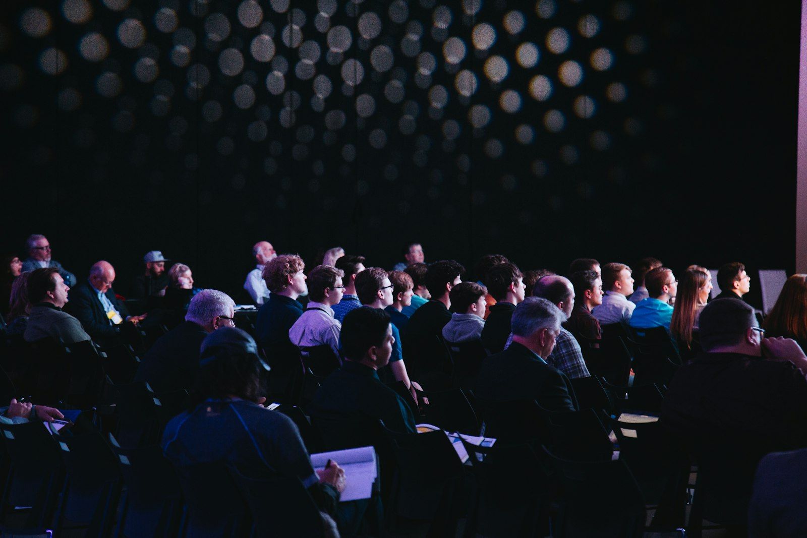 Publiczność konferencji wpatrzona w scenę w przyciemnionej sali