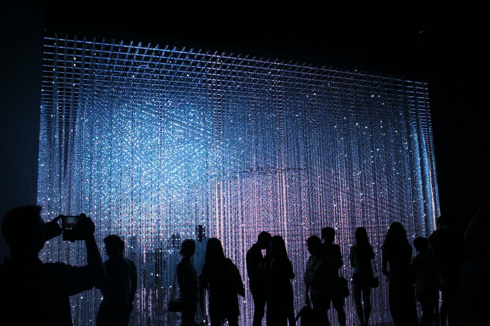 Sylwetki ludzi przed świetlną instalacją w ciemnej sali